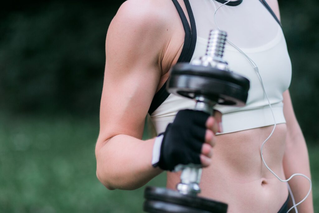 Attractive strong woman sportswear holds dumbbells her arms standing outside