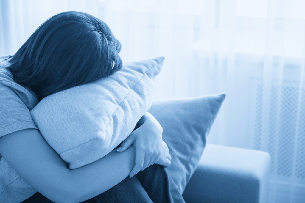 Woman sitting on couch and hugging a pillow, loneliness and sadness concept